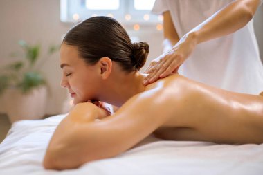 Spa 'da masaj masasında uzanan, masaj terapistinden sırt masajı alan rahat bir kadın.