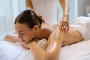 Sırtını ovmaktan hoşlanan genç bir kadın, spa terapistlerinin elleri cildini nazikçe temizlemeye ve yumuşatmaya çalışıyor. Vücut bakımı kavramı