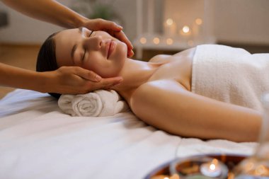 Masöz, genç bayan için rahatlatıcı yüz masajı yapıyor. Huzurlu kadın, modern lüks kaplıcalarda rahatlama tedavisi görüyor.