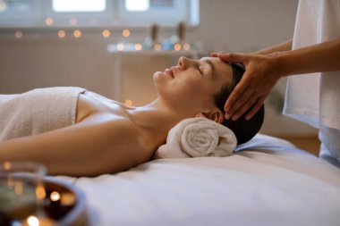 Spa merkezinde kafa masajı yapan, modern güzellik stüdyosunda akupunktur tedavisinin keyfini çıkaran, kapalı gözlerle masada uzanan rahat bir kadın.