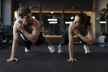 Güçlü erkek ve kadın spor salonunda yan yana şınav çekiyorlar, odaklanmış ve motive olmuş bir çift spor salonunda egzersiz yapıyor ve birbirlerine bakıyorlar.