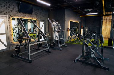 Spor salonu çeşitli halter makineleri ve kardiyo ekipmanlarıyla geniş bir düzene sahip, fitness ve sağlık odaklı iyi ışıklandırılmış iç mekanlara sahip.
