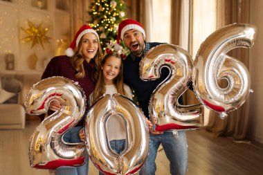 Mutlu bir aile Noel 'i evde kutluyor, 2026 numaralı dev balonları tutarak eğleniyor.