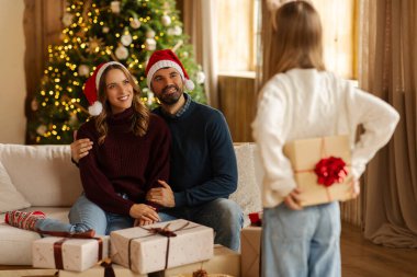 Noel arifesinde, Noel arifesinde oturma odasındaki koltukta oturan anne ve babaya Noel sürprizi hazırlayan bir kız.