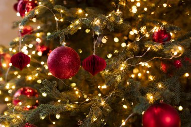 Kırmızı süslemeler ve parlak ışıklarla süslenmiş Noel ağacının yakın görüntüsü, canlı dekorasyonlar sıcak festival atmosferi yaratıyor.