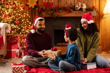 Neşeli siyah aile, Noel ağacının etrafında Noel Baba şapkaları takıp Noel Baba 'nın oğluna hediye vermek için toplanıyor.