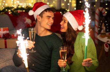 Kadın ve erkek yeni yılı kutluyorlar, ellerinde mum çeşmeleri ve şampanya bardakları, evinde oturmuş birbirlerine gülümsüyorlar.