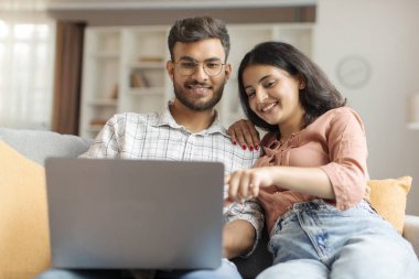 Pozitif Hintli çift dizüstü bilgisayar satın alma ya da internetten alışveriş yapıyor, film seçiyor, internette sörf yapıyor, tatil veya planlama gezisi yapıyor, birlikte kanepede oturuyor.