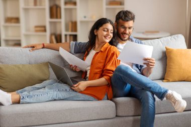 Mutlu Hintli eşler kağıtları kontrol eder ve aile bütçesini sayar, sigorta belgelerini okur, dizüstü bilgisayar kullanır, oturma odasındaki kanepede otururlar.