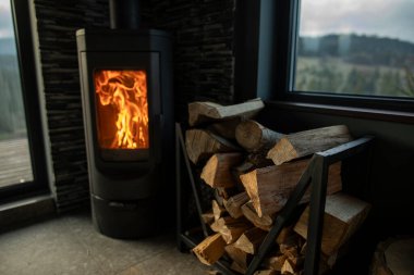 Konforlu ev odasının yanındaki odun yığınına odaklanın. Tepeleri, ormanı ve dağları gösteren geniş pencereli odun yığınına.