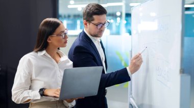 Başarılı iş arkadaşları buluşup iş hakkında konuşuyor, proje yapıyor, çalışanlar beyaz tahtada çözümü tartışıyor ve dizüstü bilgisayar kullanıyor.
