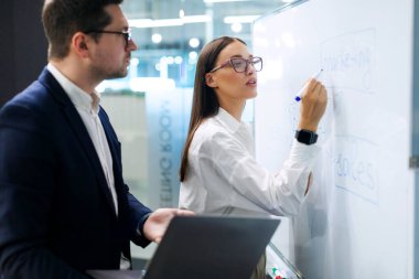 İş adamları bilgi toplamak, verileri analiz etmek, ürün geliştirmek için çözümler önermek, beyaz tahtanın yanında duran adam ve kadın.