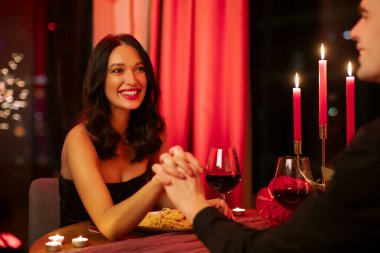 Makarna ve kırmızı şarapla yemekten hoşlanan çift, mumlar sıcak ışık ve samimi atmosfer yaratıyor, kadın ve erkek sohbet sırasında el ele tutuşuyorlar.