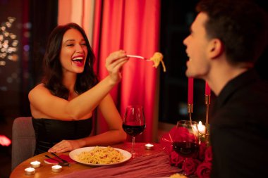 Makarna ve besleyen adamla çatal tutan mutlu bir kadın. Sevgililer gününde restoranda romantik bir akşam yemeği yiyen bir çift.