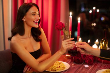 Romantik hediye. Erkek arkadaşı restoranda romantik bir buluşmada heyecanlı güzel kıza kırmızı bir gül veriyor.