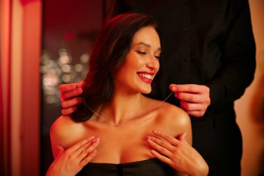 Özel Günü kutluyoruz. Mutlu genç kadınına mücevher kolye takan bir adam Sevgililer Günü 'nde romantik bir akşam yemeği yiyen bir çift.