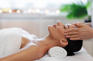 Kafa masajından hoşlanan sakin bir bayan, kozmetoloji dolabında ya da kaplıcada sağlık günü geçiriyor, masaya uzanıyor, yan gözle bakıyor.