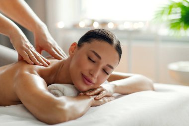 Rahatlamış sakin bir kadın, lüks spa salonunda vücut masajı yaptırıyor, profesyonel terapist kadını ovuyor, ona rahatlatıcı bir masaj yapıyor.