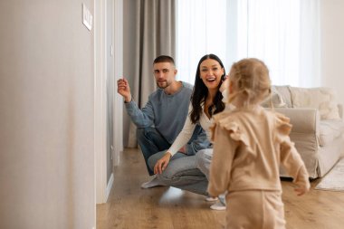 Anne babalar küçük kızlarını oturma odasındaki duvarın yanında boyunu ölçmek için çağırıyorlar.