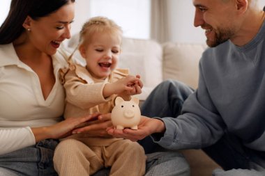 Mutlu ebeveynler küçük kızlarını para biriktirmek için eğitiyorlar. Para tutan çocuklar, gelecek eğitim için yatırım yapan aileler, gülümseyen, gülen