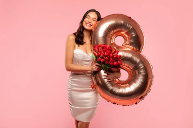 Çekici Avrupalı kadın çiçeklerle sarılmış 8 numaralı balonla Pembe stüdyo arka planında Kadın Günü 'nü kutluyor.