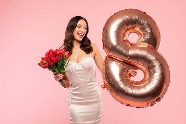 Uluslararası Kadınlar Günü. Zarif elbiseli güzel bir bayan elinde bir buket lale ve pembe arka planda sekiz numaralı balon tutuyor.