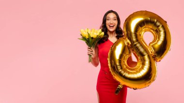 Heyecanlı bir bayan elinde bir buket lale ve 8 numaralı balon ile bahar tatilini kutluyor. Pembe arka planda poz veriyor. Kopya alanı olan bir panorama.