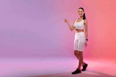 Şuraya bak. Spor kıyafetli bayan fotokopi alanını işaret ediyor. Pembe ve şeftali rengi gradyan arka plan için fitness reklamı yapıyor.