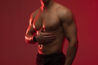 Unrecognizable strong athletic man with muscular naked torso touching his chest, posing over red studio background. Sport and bodycare concept