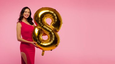 Pembe arka planda poz veren ve şekil 8 şeklinde altın renkli balonu olan mutlu genç bir kadın. Uluslararası Kadın Günü