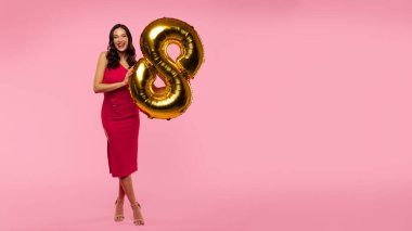 Zarif elbiseli mutlu bir bayan elinde 8 numaralı balonla Kadın Günü 'nü kutluyor pembe arka planda poz veriyor.