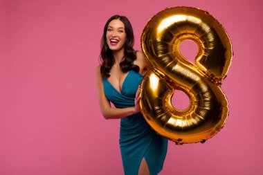 Uluslararası Kadınlar Günü. Pembe stüdyo arka planında poz veren, elinde 8 numaralı balon tutan heyecanlı bayan.