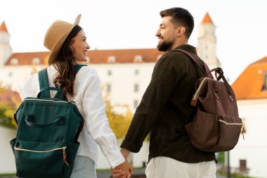 Tarihi bölgede birlikte yürüyen, el ele tutuşan ve birbirlerine gülümseyen iki turist sırt çantalı, dikiz aynasından