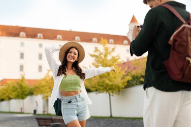 Mutlu çift eğleniyor, yeni şehri keşfediyor, kadın mutlu poz veriyor erkek kamerada fotoğraf çekerken.