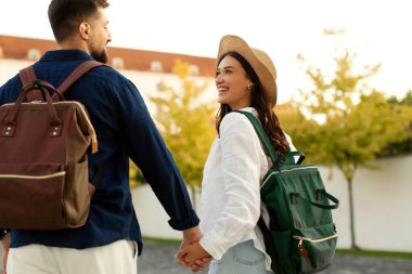 Günbatımında tarihi bölgede el ele tutuşan mutlu turistler, sırt çantaları taşıyan erkek ve kadın, şehri keşfediyorlar.