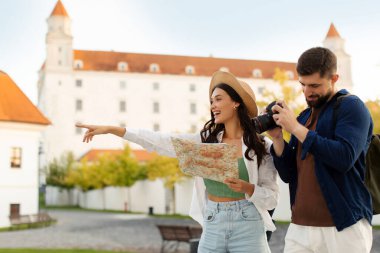İki mutlu turist adam ve kadın, tarihi yerleri ziyaret ederek eğleniyorlar. Kadın, erkek fotoğraf çekerken bir şeye işaret ediyor.