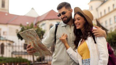 Tarihi şehirde haritaya bakan mutlu çift, bayanı kucaklayan ve gülümseyen adam, bir sonraki aktivitelerini planlayan, yolculuğun tadını çıkaran.