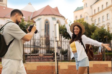 Gülümseyen ve poz veren mutlu kadının fotoğrafını çeken adam, tarihi şehir simgelerinde yürüyen çift.