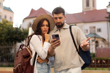 İki kayıp turist rehberlik için cep telefonuna bakıyor, şehir içinde yürürken tarihi binanın önünde GPS navigatörünü kullanıyorlar.