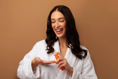 Güzel bir bayan saçı için gerekli yağ spreyini uyguluyor, bej arka planda poz veriyor. Onarım tedavi kavramını böl