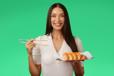 Elinde suşi dürümleri olan bir kadının portresi geleneksel Japon yemeklerini yemekten zevk alıyor ve yeşil arka planda servis hizmeti sunuyor.