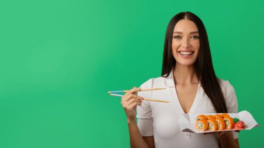 Elinde suşi dürümleri olan mutlu bir bayan geleneksel Japon yemekleri yiyen bir kadın, teslimat tavsiyesi yeşil arka planda duran, boş alanı olan bir panorama.