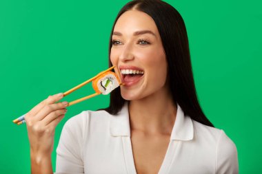 Genç bir kadının ağzını açtığı, çiğ suşi yediği, Japon yemeğinin tadını çıkardığı, yeşil arka planda dikildiği yakın plan.