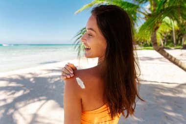 Güneş koruma kozmetik ürünleri. Bronzlaşmış omzuna güneş kremi süren bir kadın, Okyanus kıyısında duran, kopyalama alanı