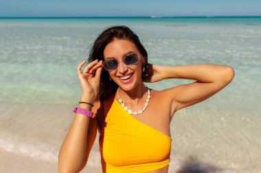 Turizm ve yaz tatili. Güneş gözlüklü ve mayo giyen mutlu kadın tropik kumlu sahilde yürüyor, adada, panoramada, boş alanda cennetin tadını çıkarıyor.