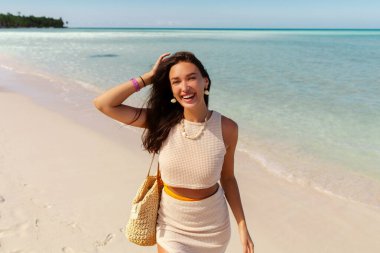 Kumsalda gülümseyen genç bir kadın, tropik bir adada tatilin tadını çıkarıyor, arka planda palmiyeler.