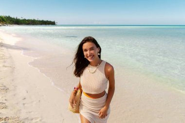 Kumsalda gülümseyen genç bir kadın, tropik bir adada tatilin tadını çıkarıyor, arka planda palmiyeler.