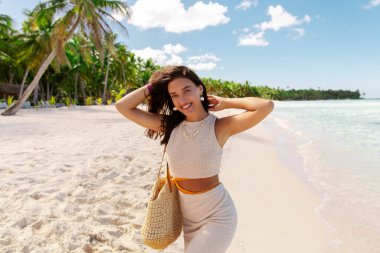 Kumsalda gülümseyen genç bir kadın, tropik bir adada tatilin tadını çıkarıyor, arka planda palmiyeler.