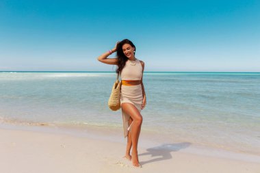 Kumsalda gülümseyen mutlu genç bir kadın, tropik bir adada tatilin tadını çıkarıyor, arka planda avuçlar, uzun bir çekim.