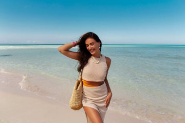 Kumsalda gülümseyen genç bir kadın, tropik bir adada tatilin tadını çıkarıyor, arka planda palmiyeler.